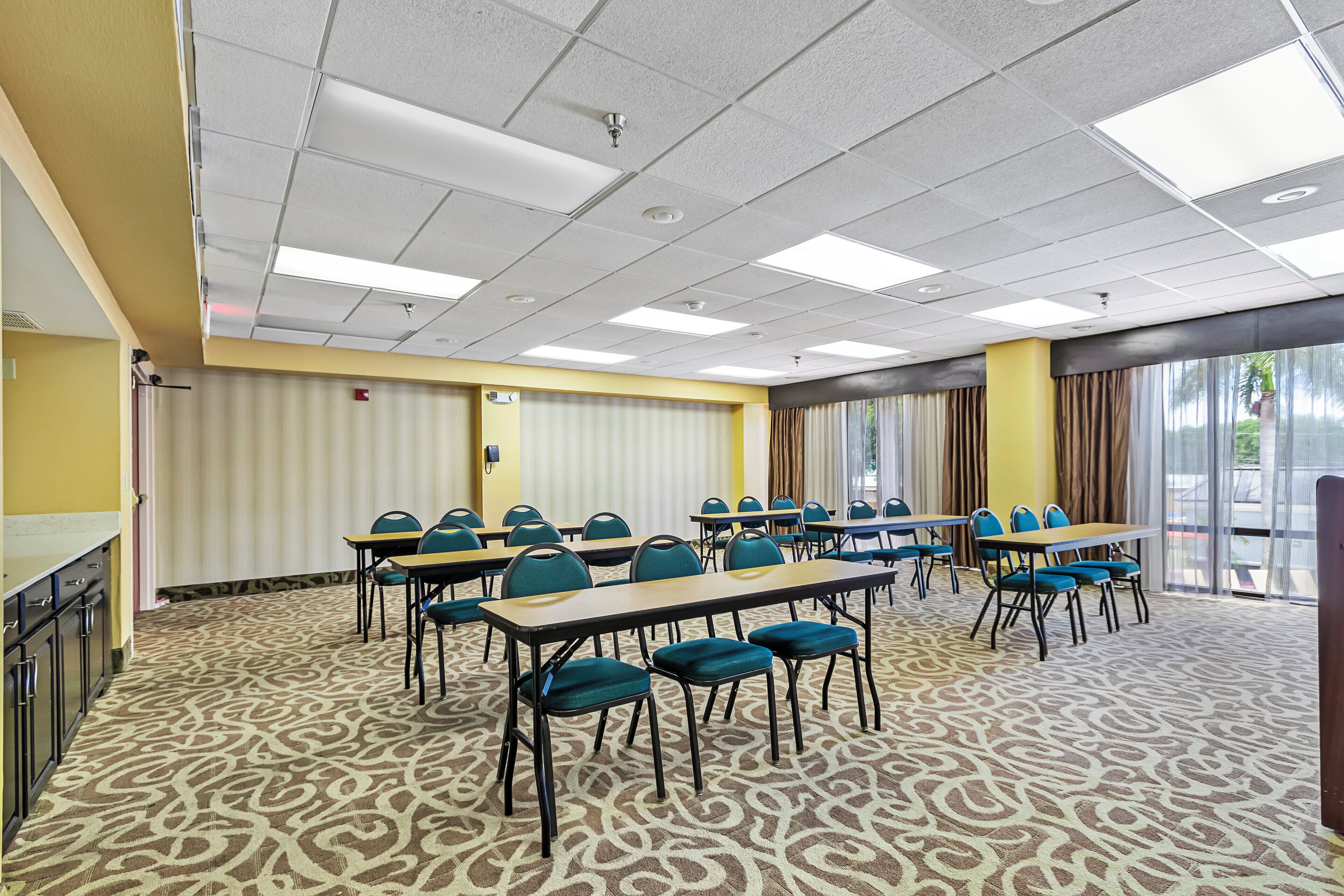 A conference room with a patterned carpet, multiple tables with chairs, and a large window with curtains.