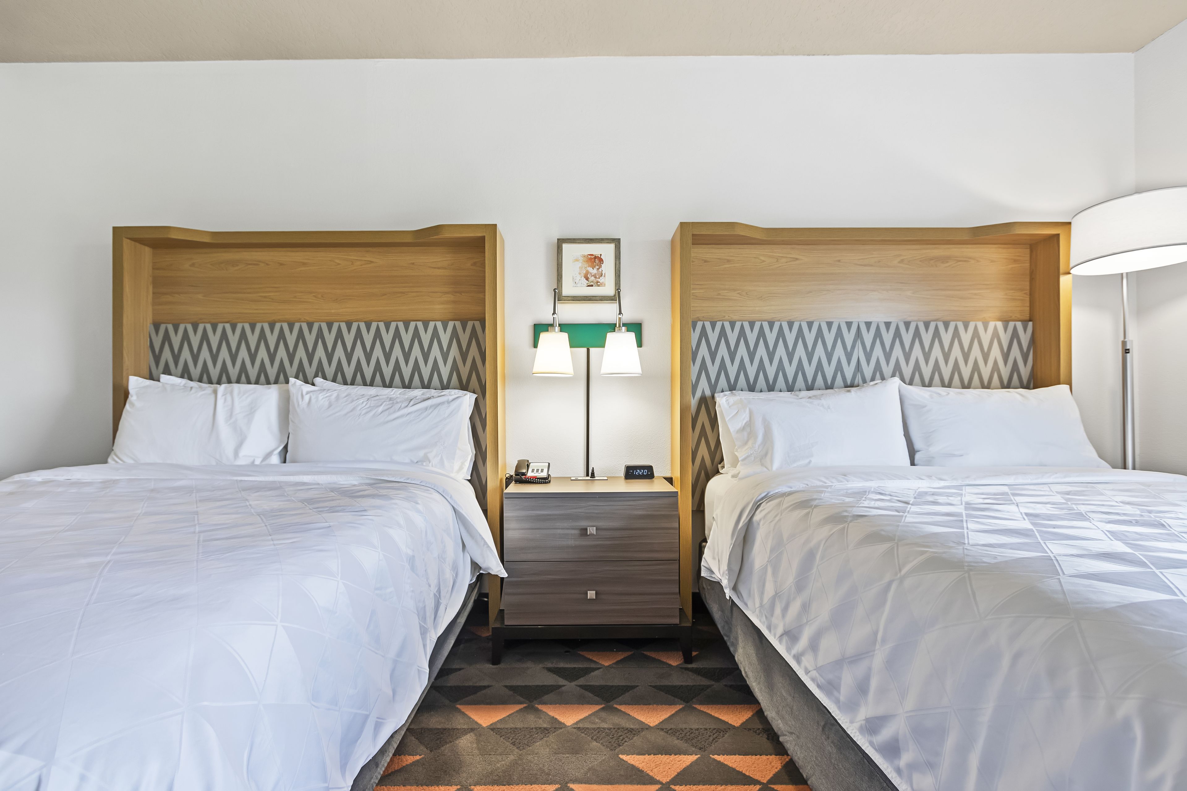 A hotel room with two beds, a nightstand with a lamp, and a patterned rug.