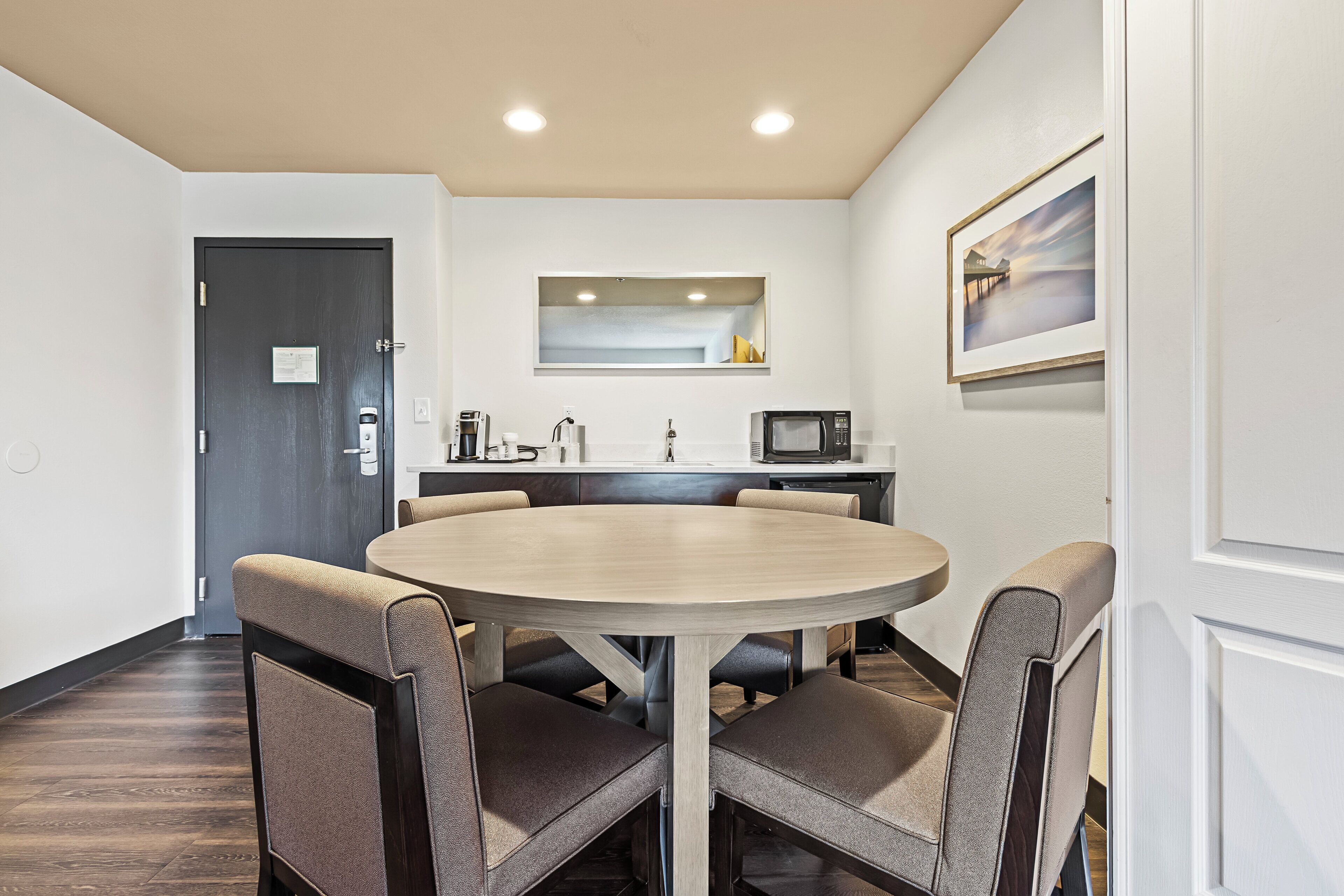 A dining area with a round table and four chairs, a kitchen area with appliances, and a framed picture on the wall.