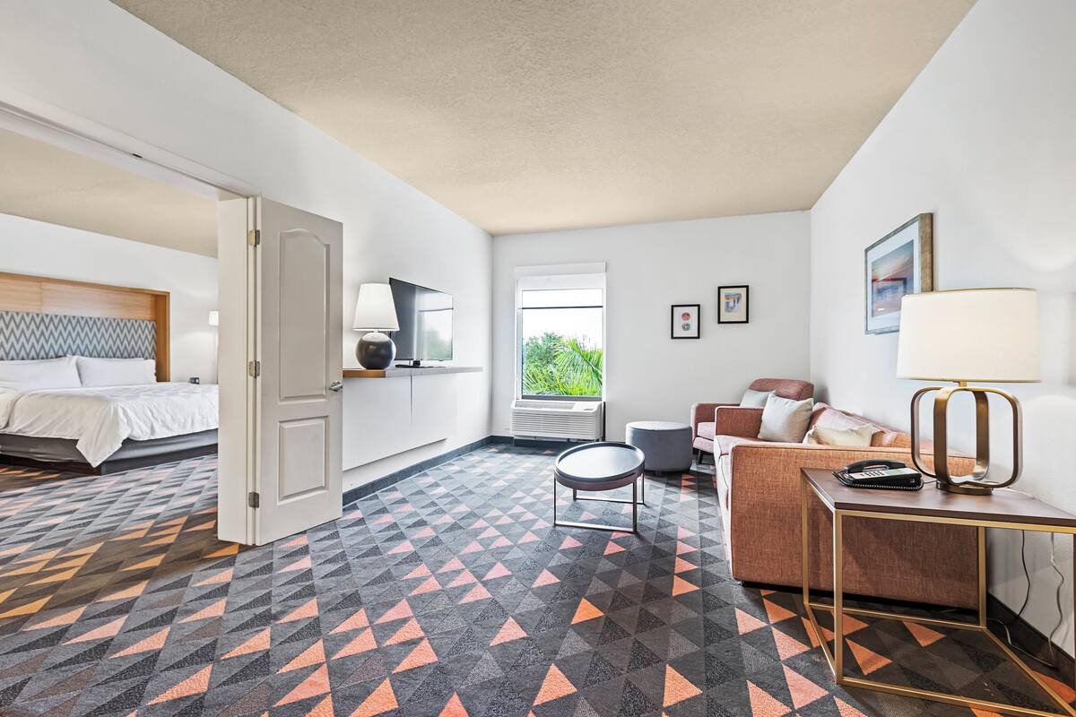 Habitación de hotel con cama, sofá, escritorio, lámpara, ventana y suelo estampado.