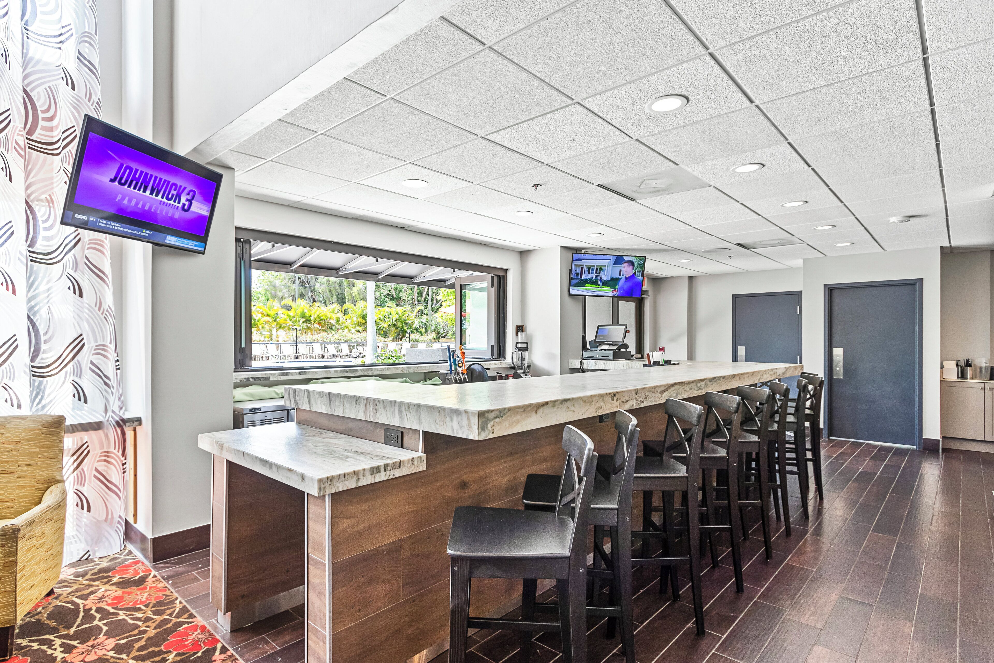 A bar area with a long counter, multiple stools, and a television screen displaying a sports event.