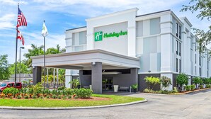 A Holiday Inn hotel with a covered entrance, flag display, and landscaped garden.