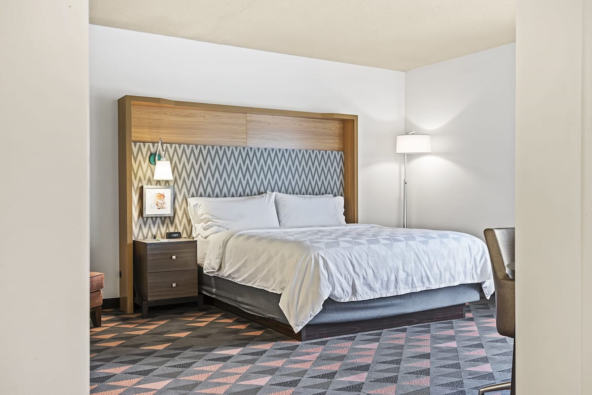 Une chambre d’hôtel bien rangée, avec un lit, une table de chevet, une lampe et un tapis à motifs.