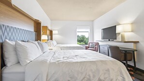 A hotel room with two beds, a desk, a chair, a TV, and a window with a view of greenery.
