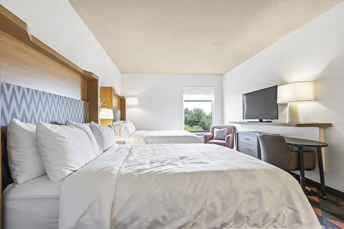 Une chambre d’hôtel avec deux lits, un bureau, une chaise, une télévision et une fenêtre donnant sur un espace verdoyant.