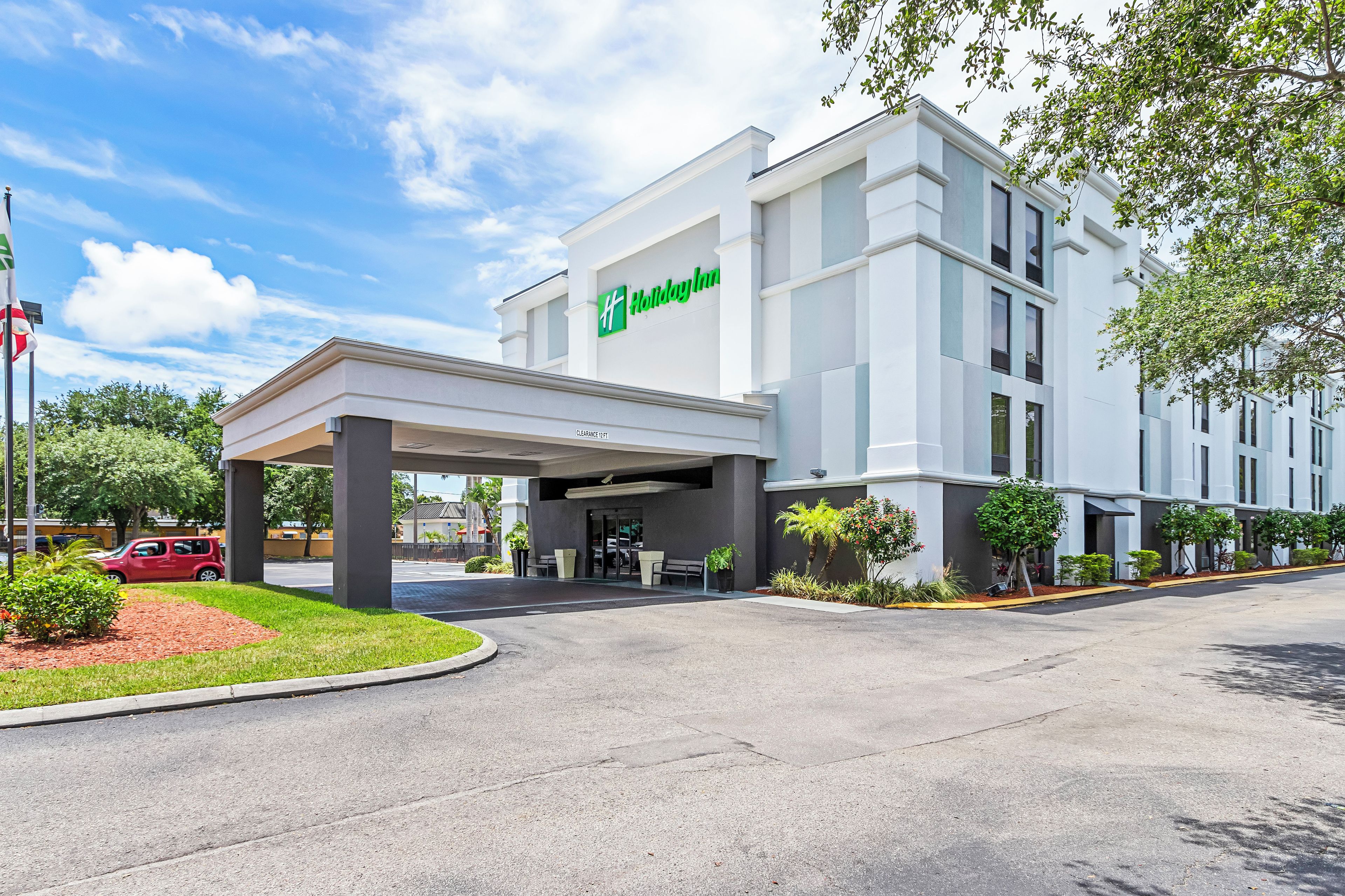 Un hotel Holiday Inn con entrada cubierta, aparcamiento y cielo despejado.