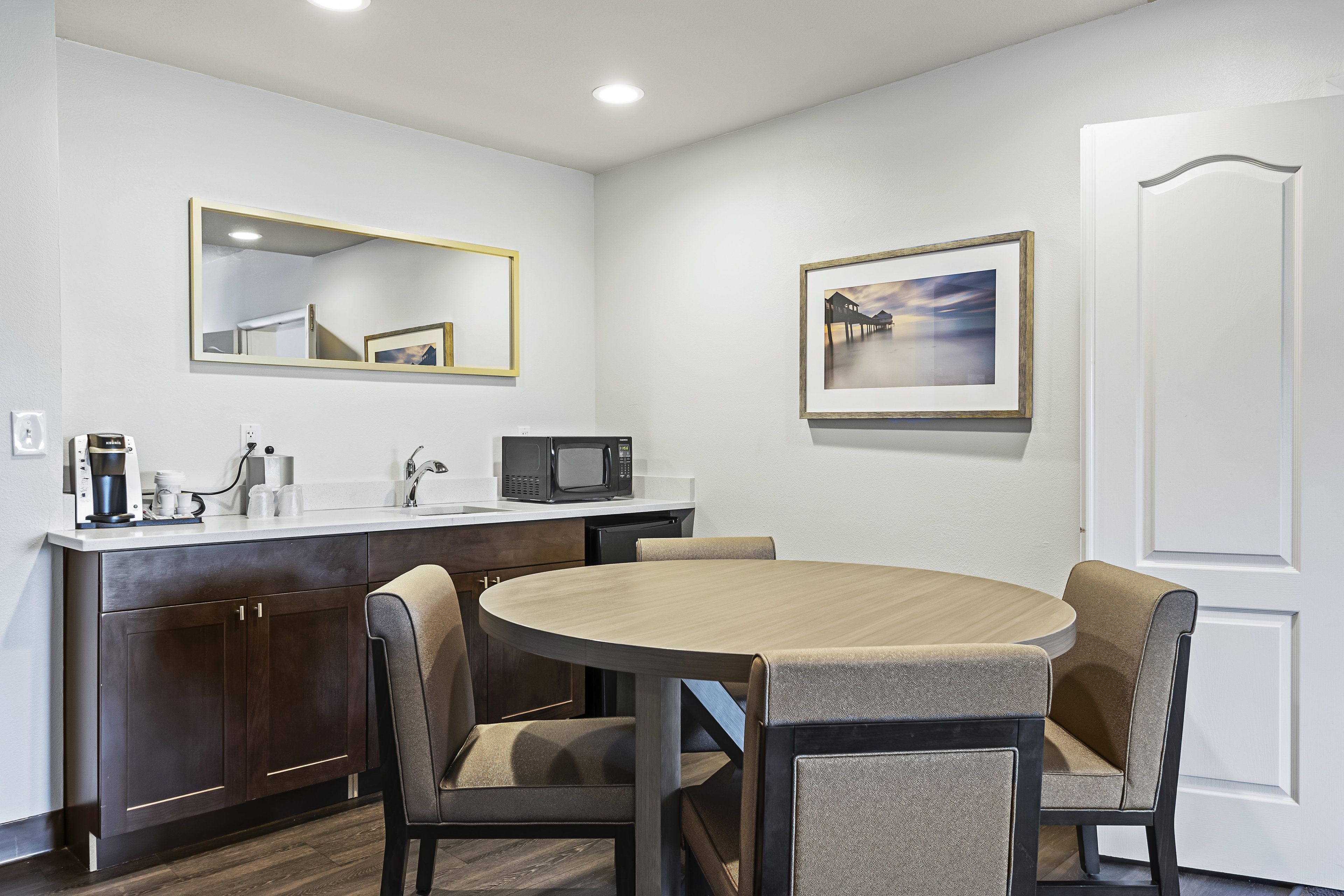 A modern kitchen with dark wood cabinets, a white countertop, a round wooden table, and two beige chairs.