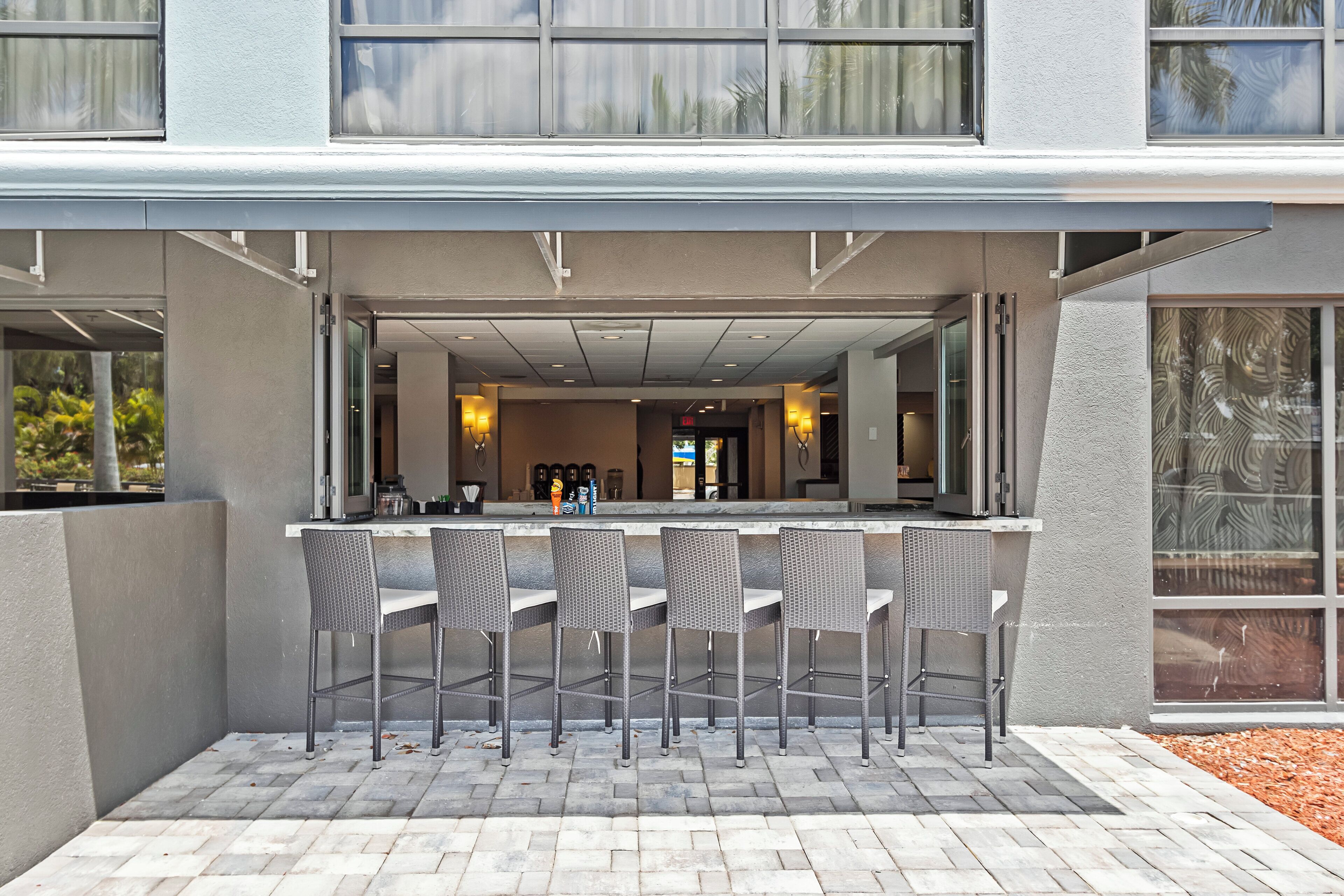An outdoor seating area with a bar and chairs, a paved walkway, and a building entrance.