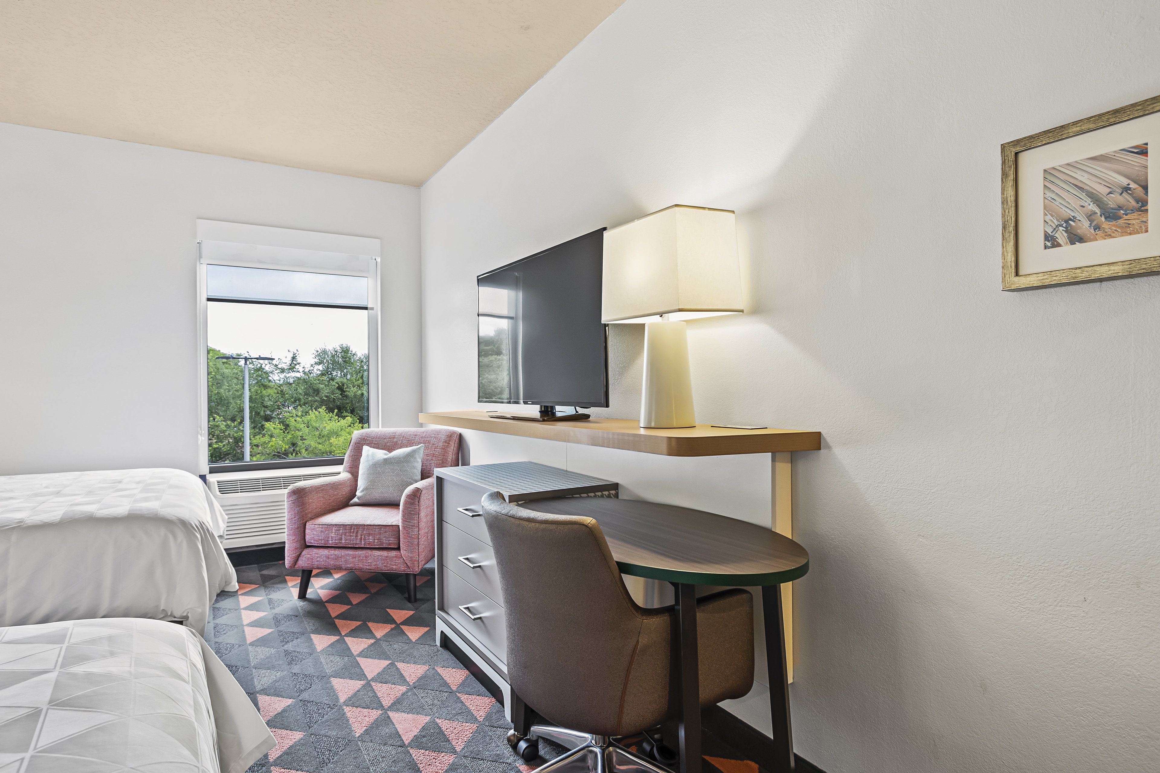 A hotel room with a bed, a desk with a chair, a television, and a lamp.