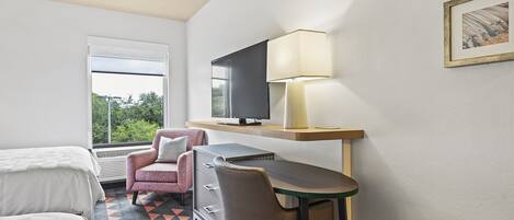 A hotel room with a bed, a desk with a chair, a television, and a lamp.