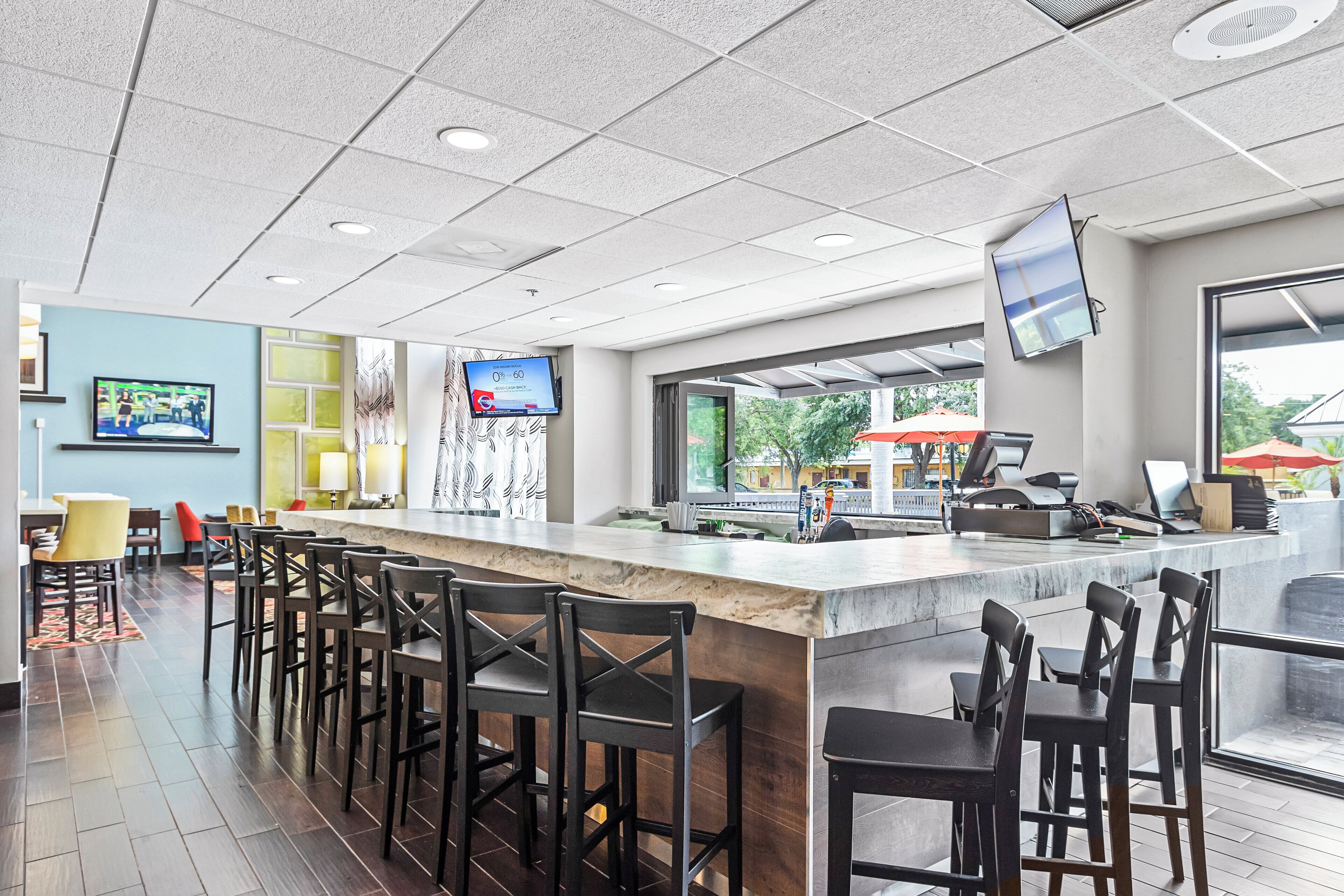A bar area with a long counter, multiple stools, and a television screen displaying an advertisement.