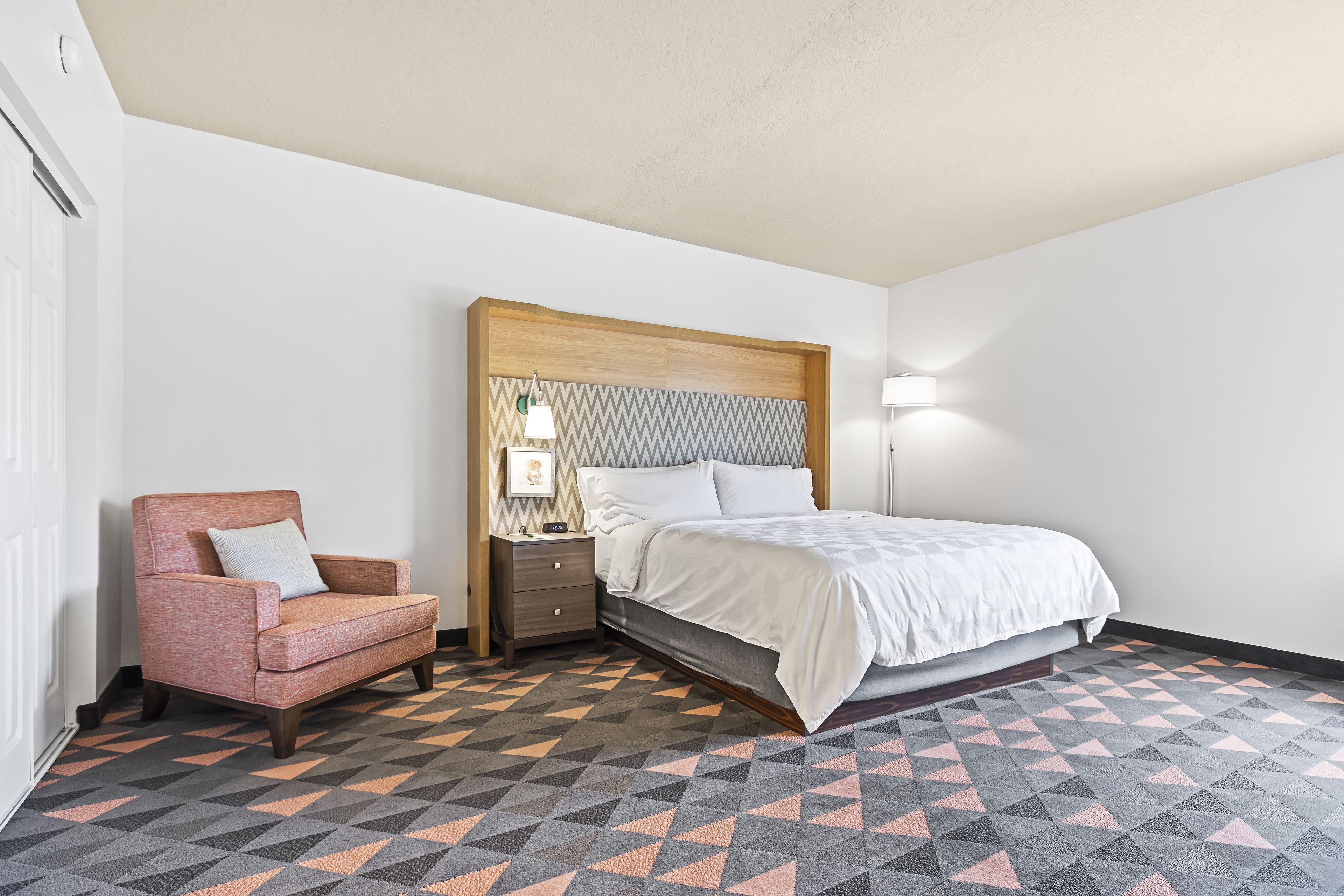Une chambre à coucher avec un lit, une table de chevet, une chaise et un sol à motifs.