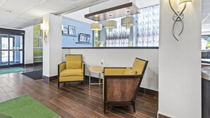 A modern lobby with a reception desk, two yellow armchairs, a dining table, and a large mirror.
