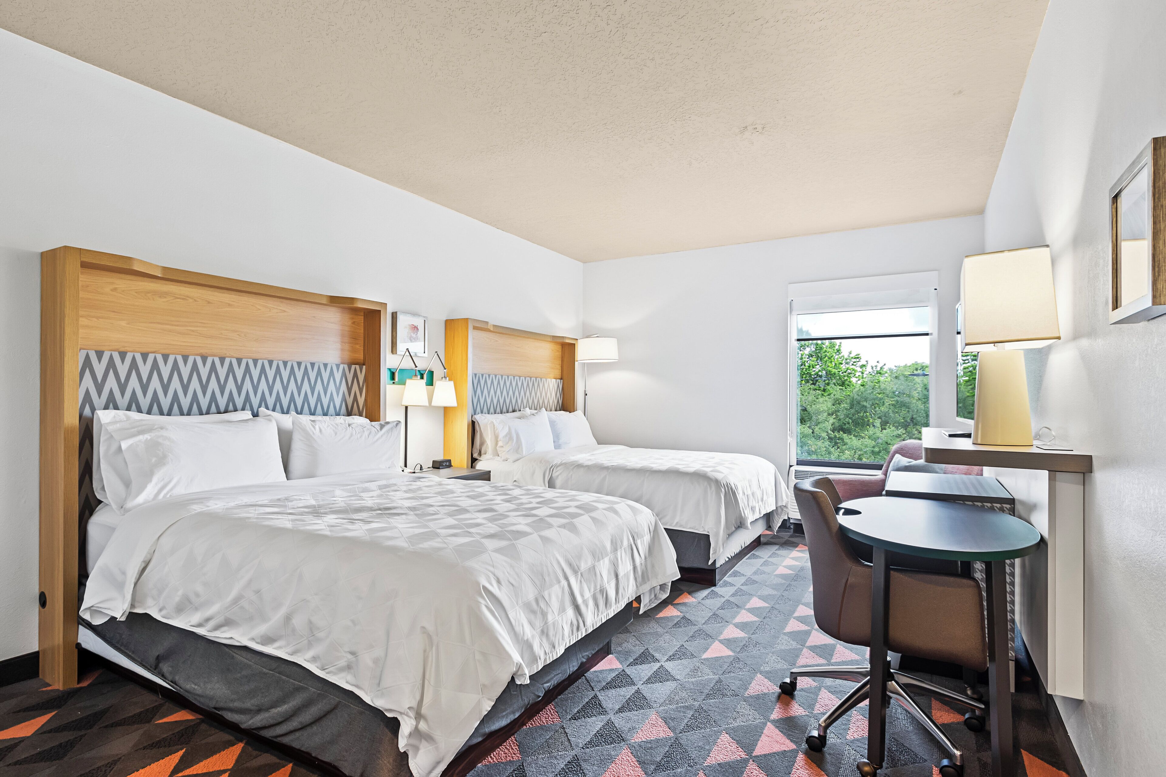 Une chambre d’hôtel avec deux lits, un bureau, une chaise et une fenêtre donnant sur un paysage agréable.