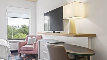 A hotel room with a bed, a desk with a lamp, a TV, and a chair.