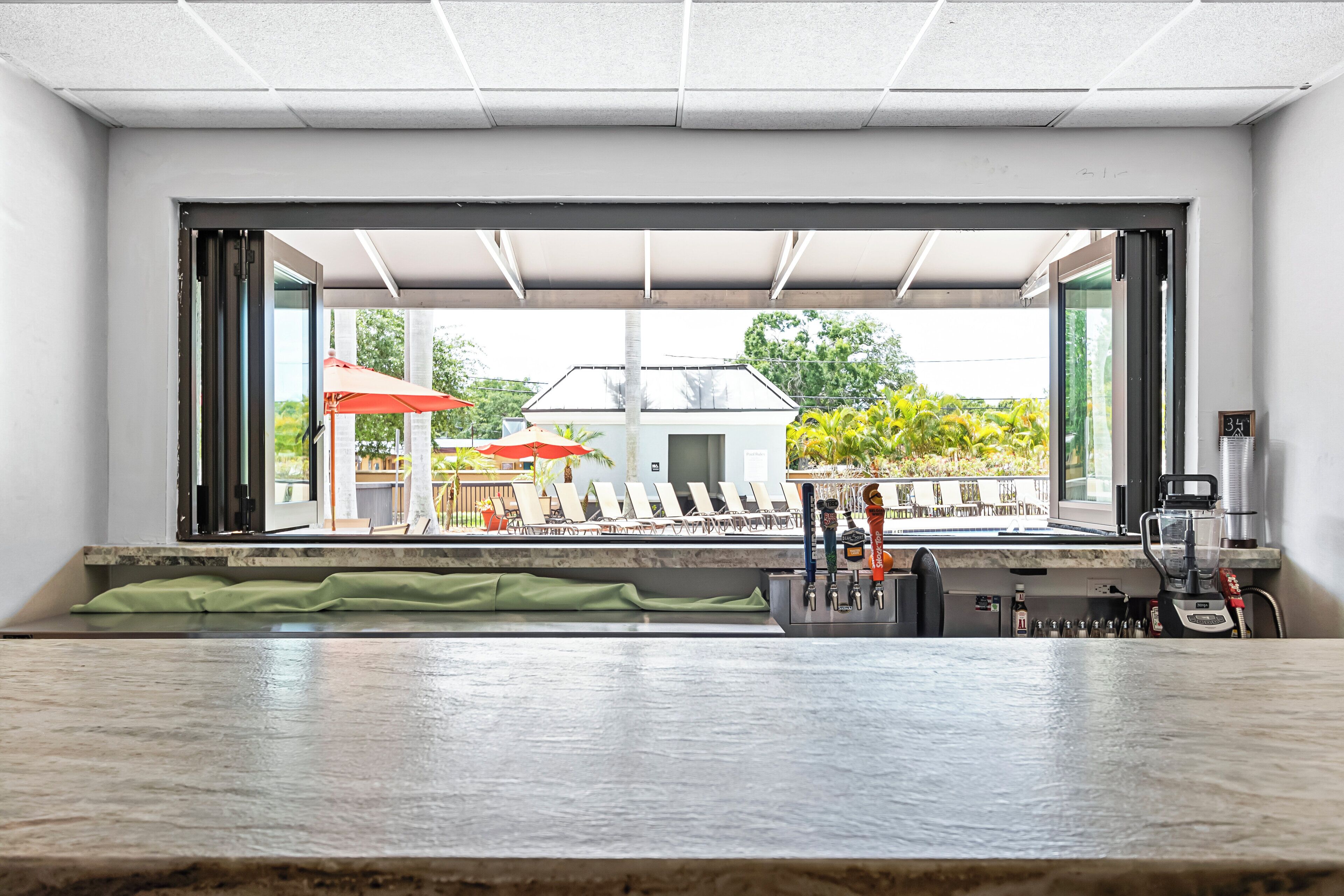 A bar area with a view of the outside, including a pool and umbrellas.