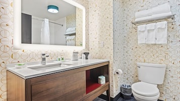 Un baño con tocador de madera, un espejo grande, inodoro y perchero para toallas.