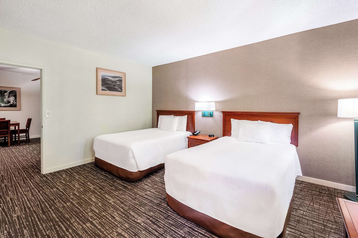 A hotel room with two single beds, a nightstand with a lamp, a framed picture on the wall, and a carpeted floor.