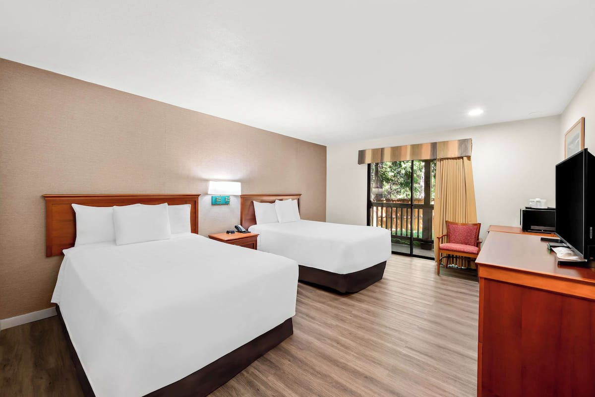 A hotel room with two beds, a desk, a chair, a TV, and a window with curtains.