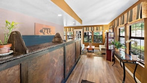 A reception area with a wooden reception desk, potted plants, a fire truck painting, and large windows with views.