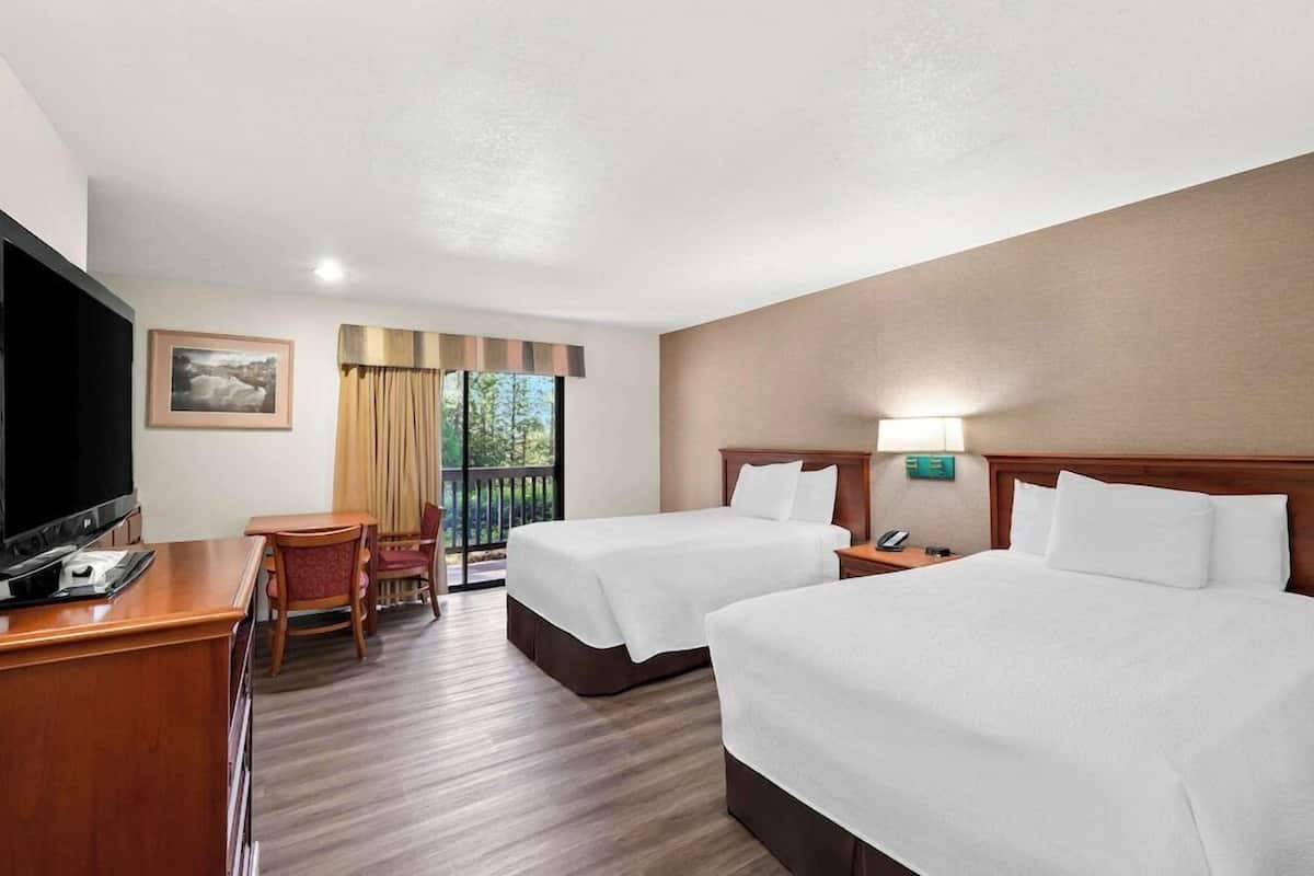 A hotel room with two beds, a desk with a TV, a chair, a window with curtains, and a nightstand with a lamp.