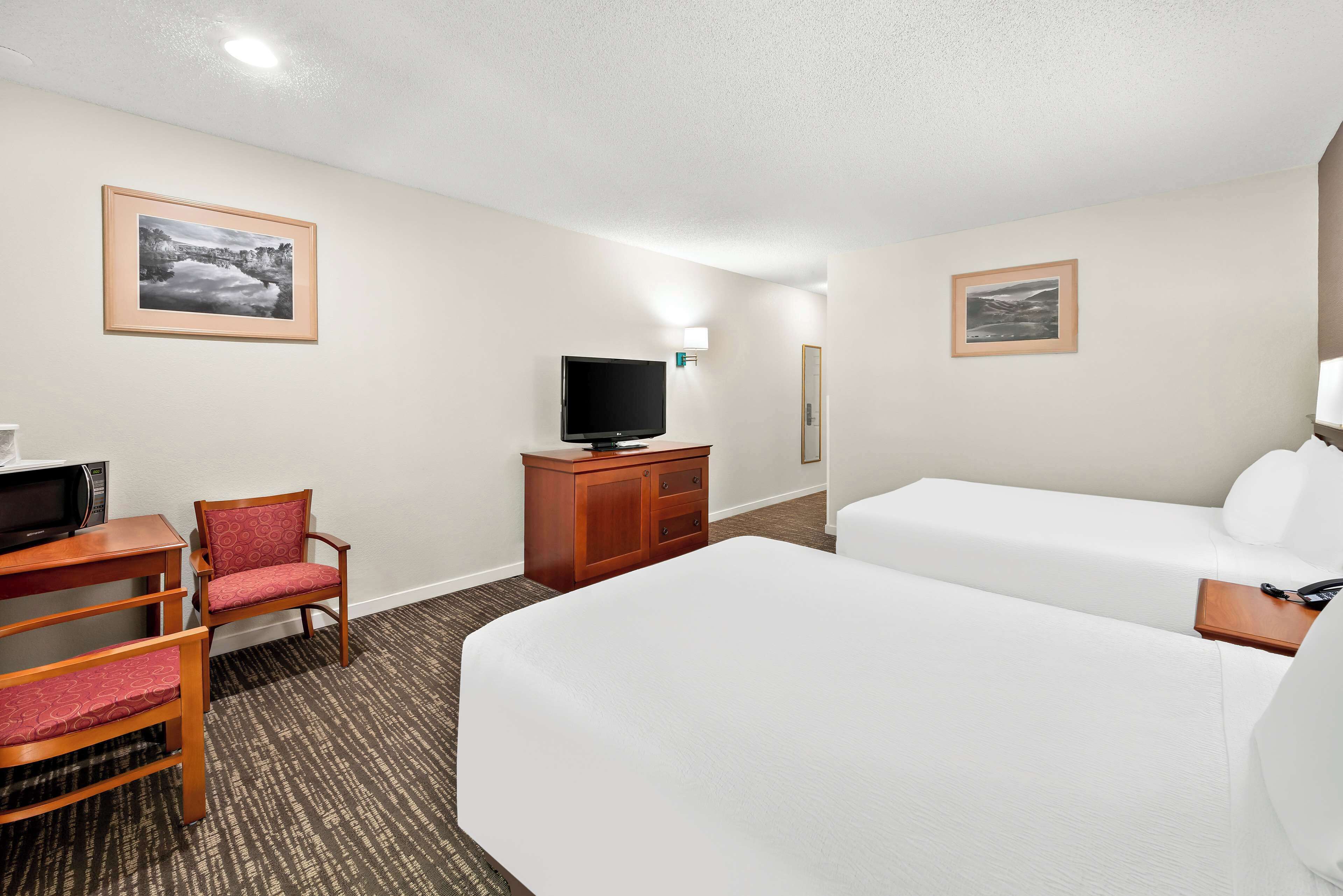 Ein Hotelzimmer mit einem Bett, zwei Sesseln, einem Fernseher und einem Schreibtisch.