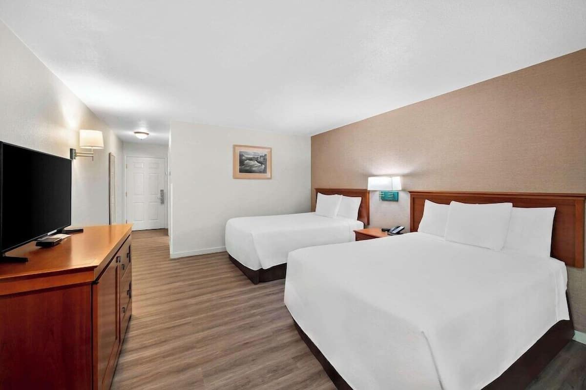 A hotel room with two beds, a TV, a desk, and a door.