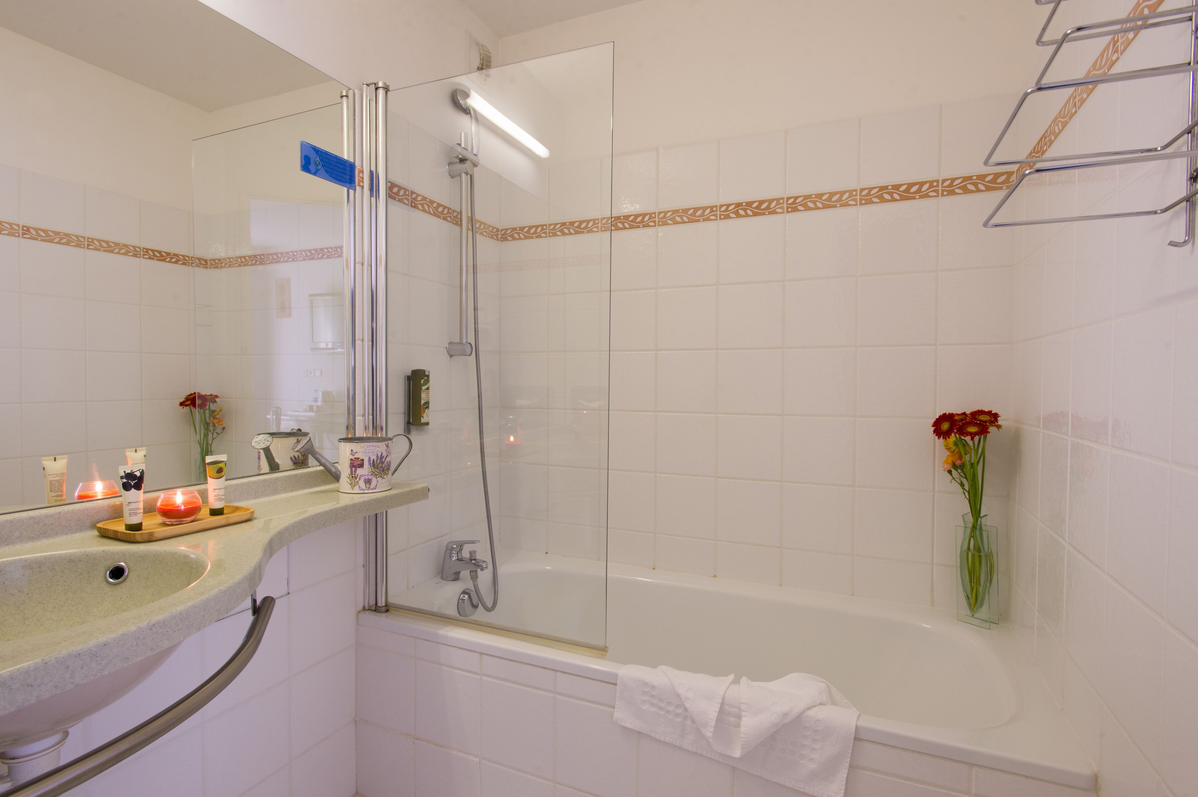 A bathroom with a glass-enclosed shower, a bathtub, a vanity with toiletries, and a towel rack.