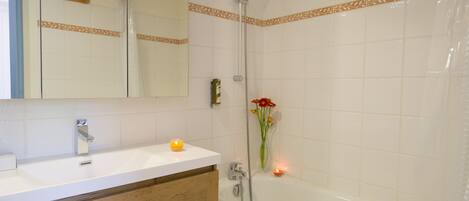 A bathroom with a white bathtub, a shower, a vanity with a mirror, and a candle on the counter.