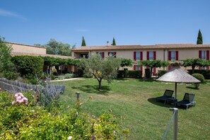 A courtyard with a building featuring red shutters, a thatched umbrella, and outdoor seating. - Best Western Aurelia (Maussane-les-Alpilles)