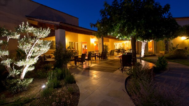 Un espace extérieur aménagé en terrasse, avec des tables et des chaises, entouré d’arbres et de plantes.