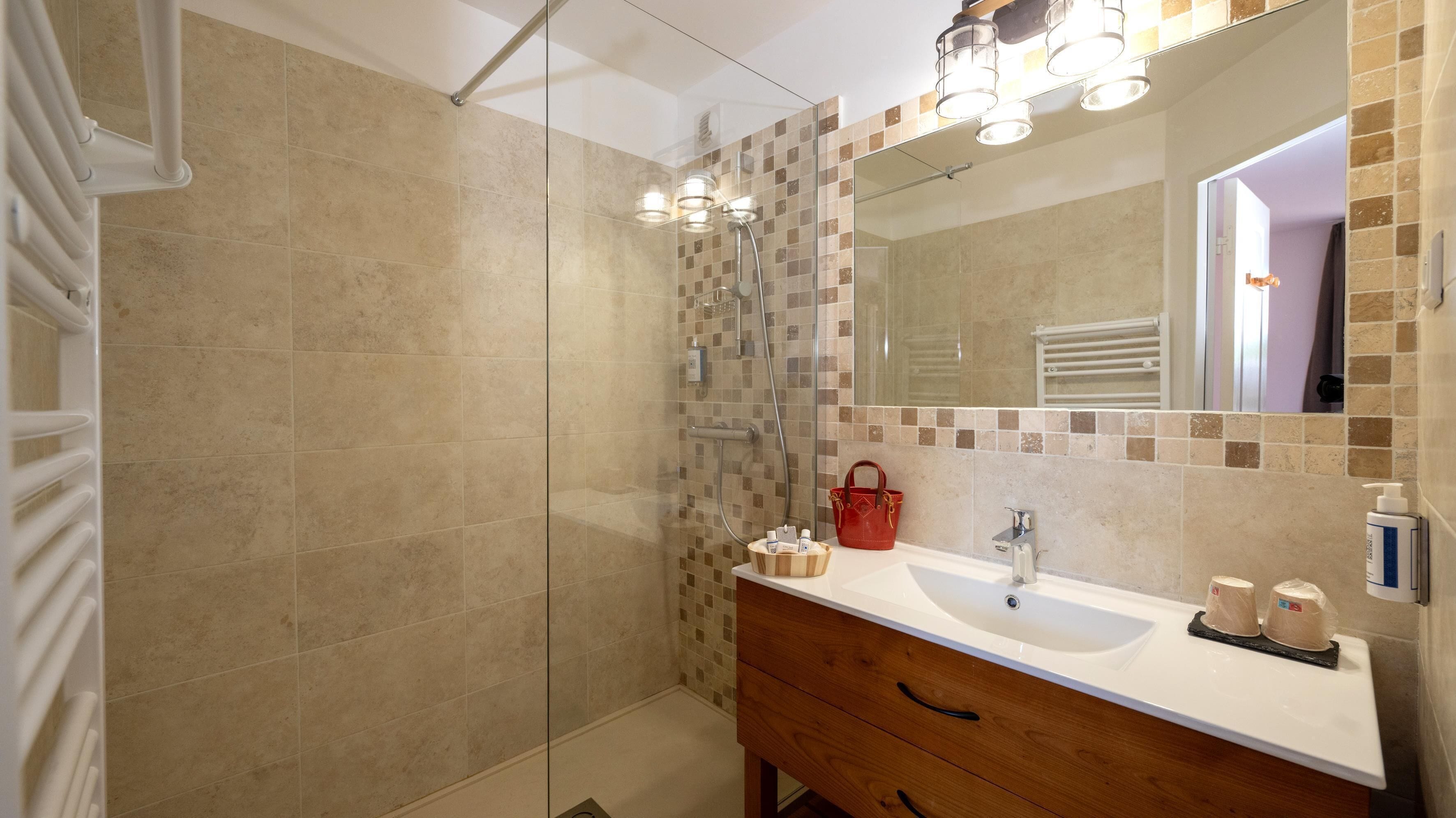 A bathroom with a shower, a sink, a mirror, and toiletries.