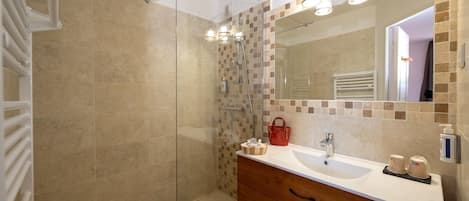 A bathroom with a shower, a sink, a mirror, and toiletries.