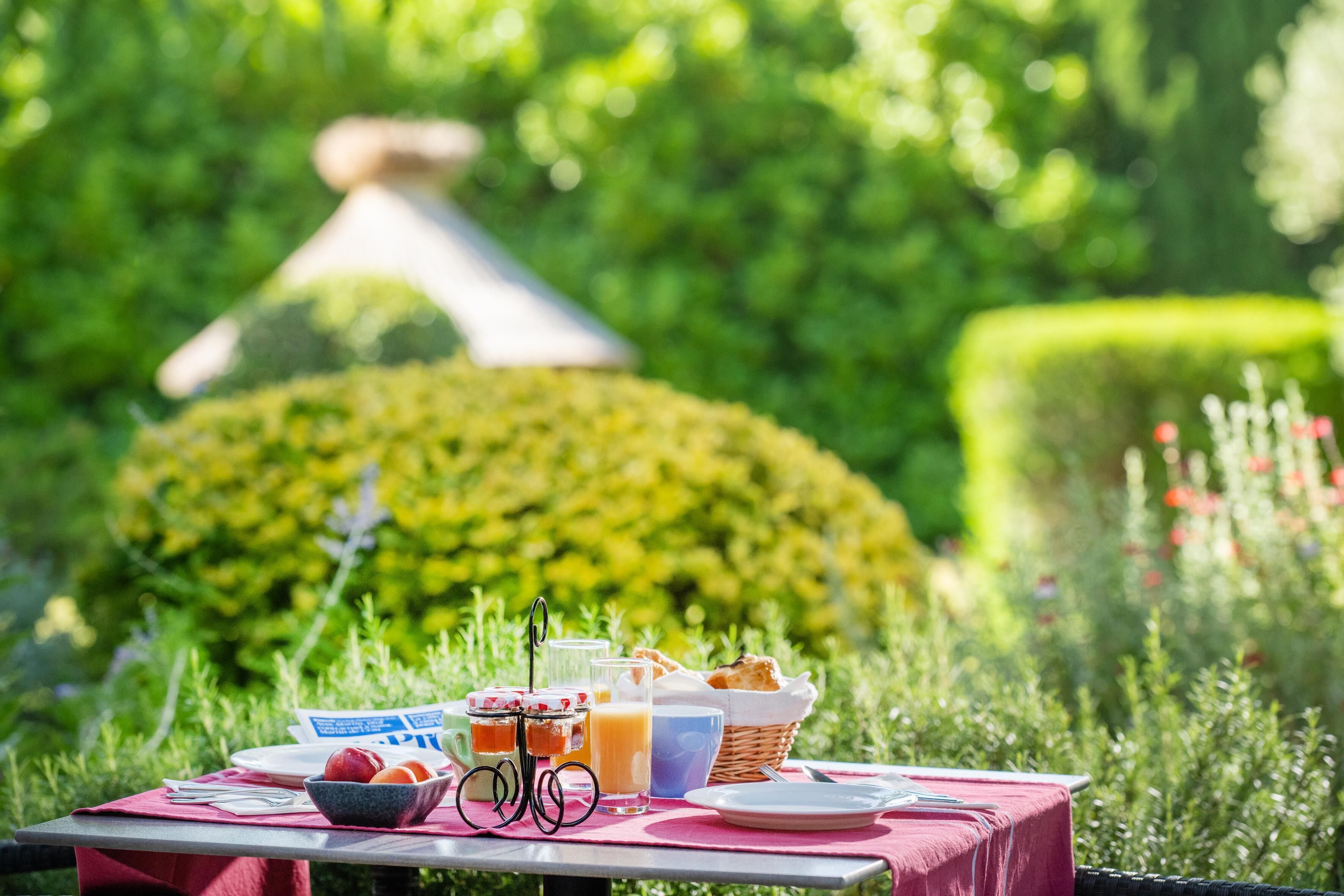 An outdoor dining table set with a picnic arrangement, including a basket, jars, and a glass of orange juice.