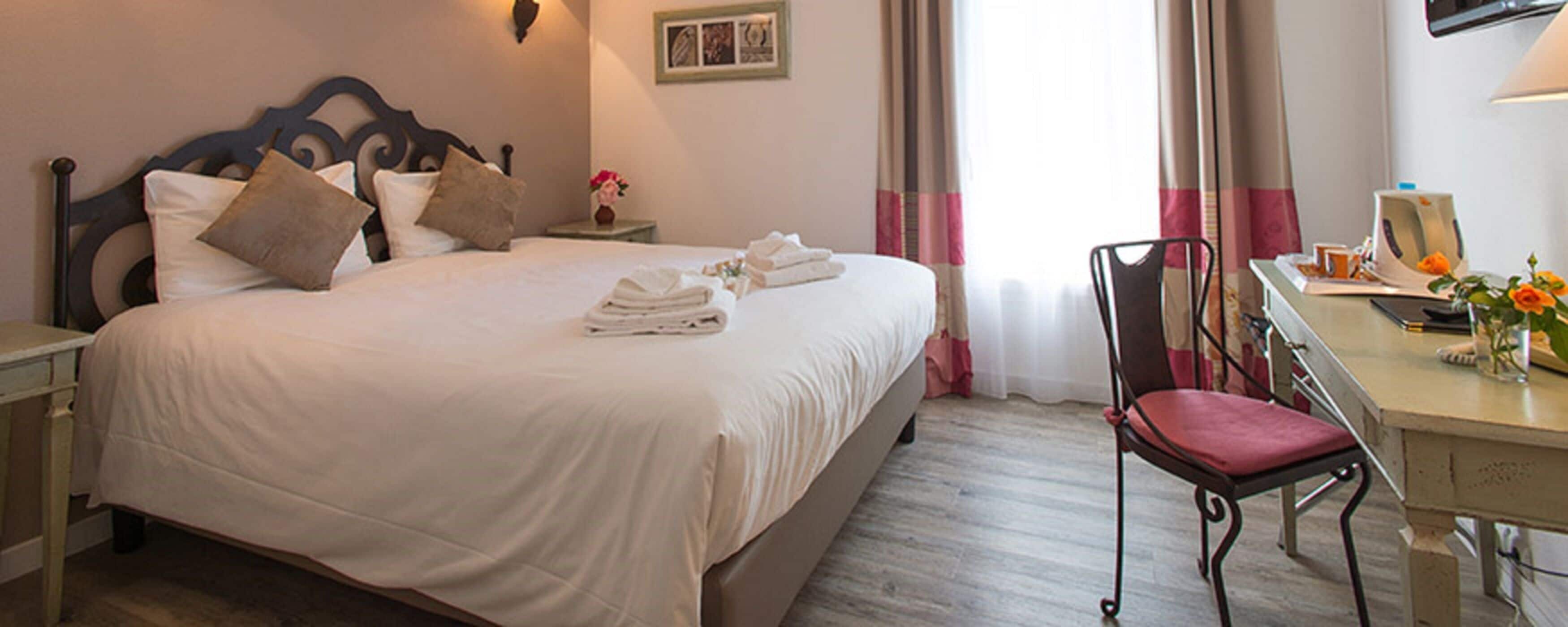 A neatly made bed with pillows and folded towels, a desk with a chair, and a picture on the wall.