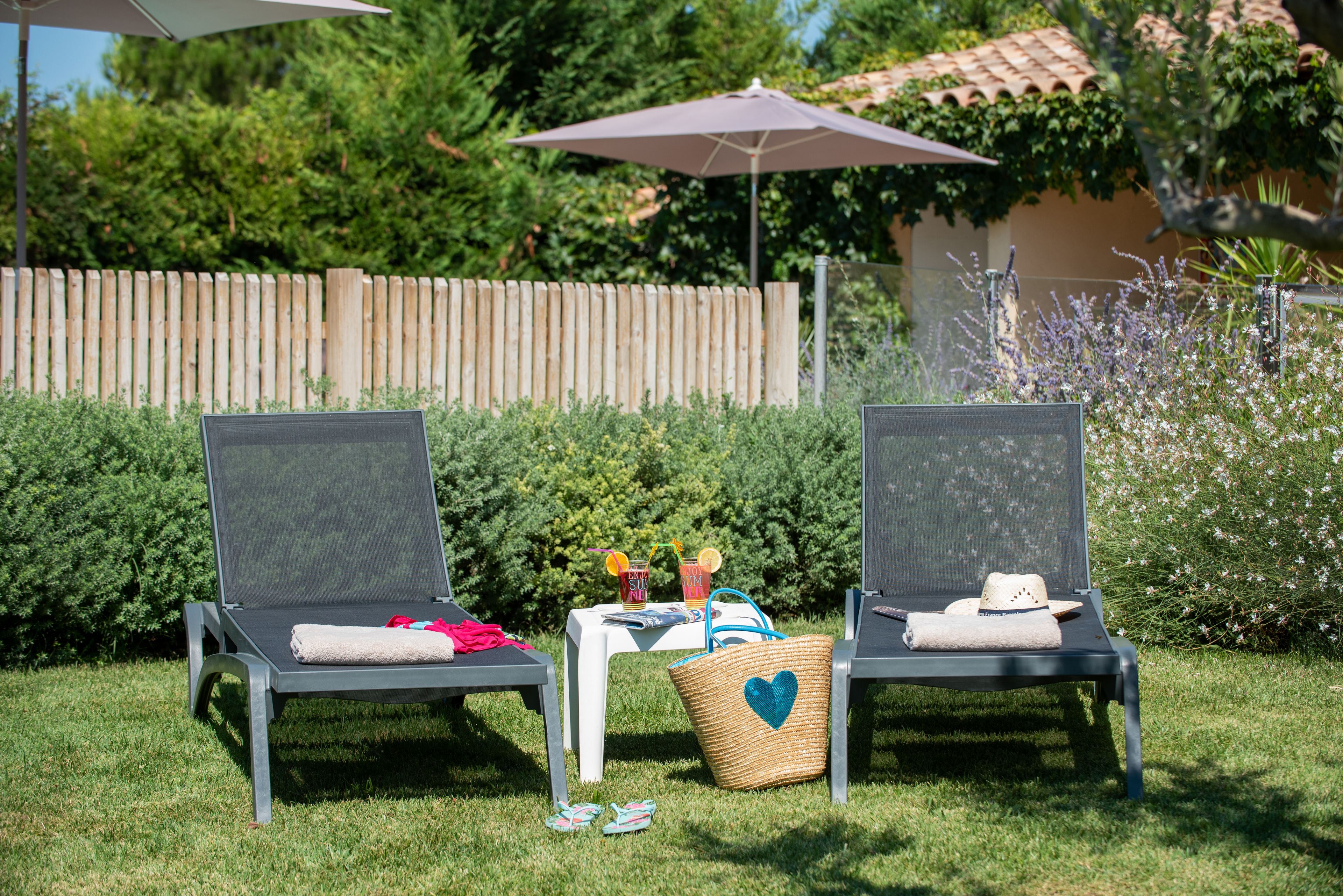 Two outdoor lounge chairs with a table between them, a basket with a heart design, and a wooden fence in the background.