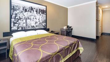 A hotel room with a large bed, a cityscape artwork on the wall, a desk with a chair, and a nightstand.