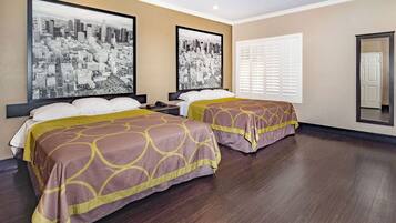 A hotel room with two beds, a large window with blinds, and two cityscape photographs on the wall.