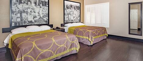 A hotel room with two beds, a large window with blinds, and two cityscape photographs on the wall.