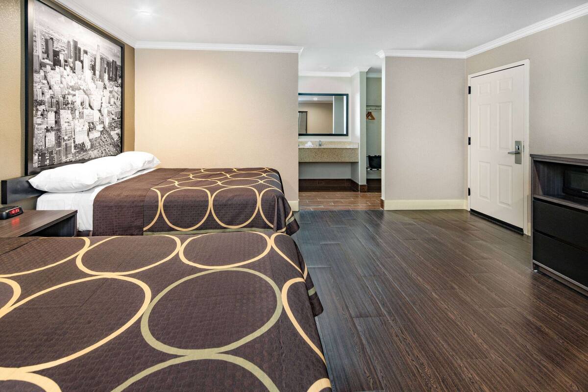 A hotel room with two beds, a large framed cityscape picture, a nightstand, and a wooden floor.