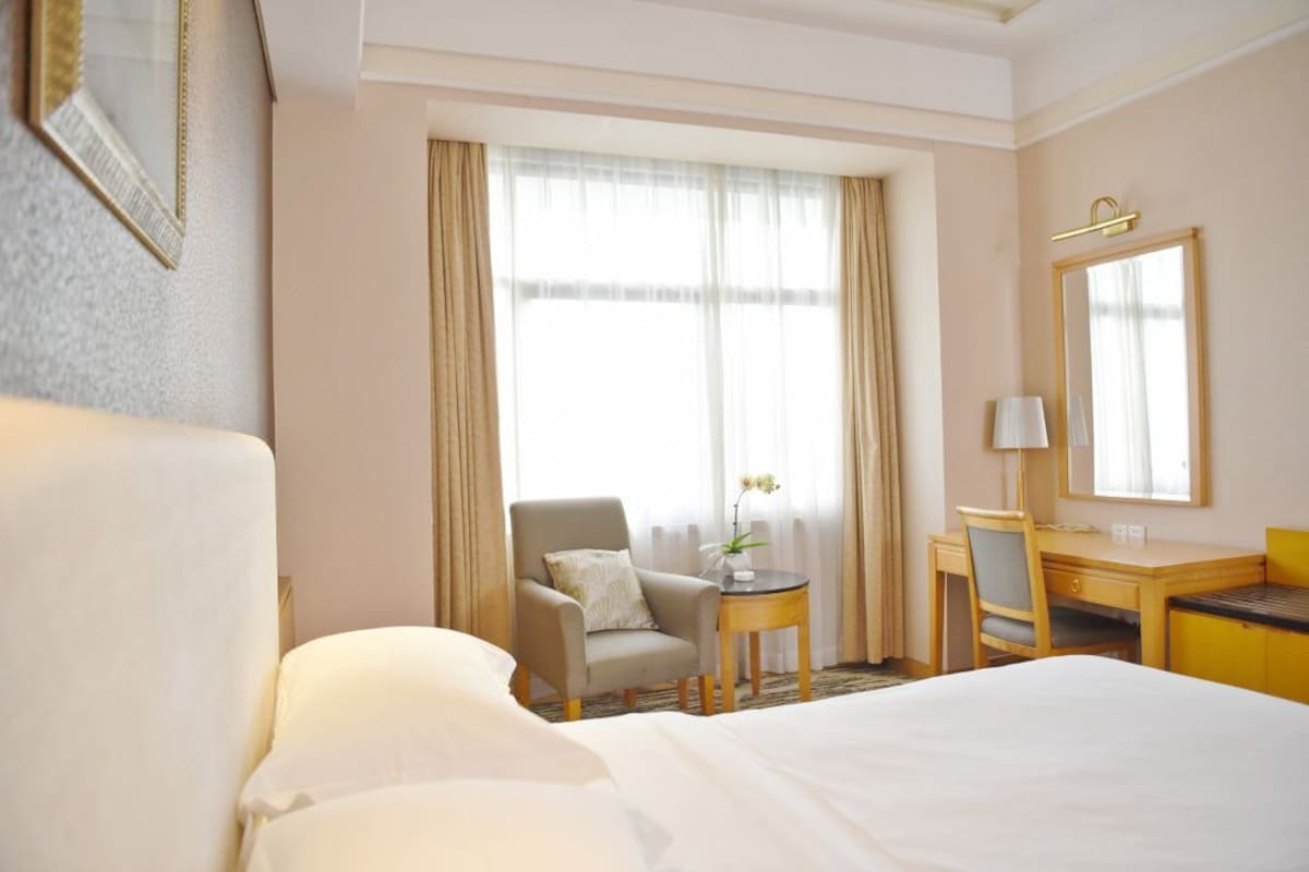 A hotel room with a large bed, a desk, a chair, and a window with curtains.