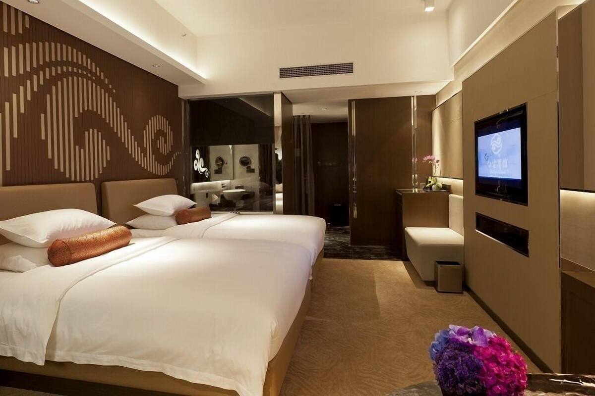 Une chambre d’hôtel moderne, dotée d’un grand lit, d’une télévision et d’une salle de bain visible à travers une porte ouverte.
