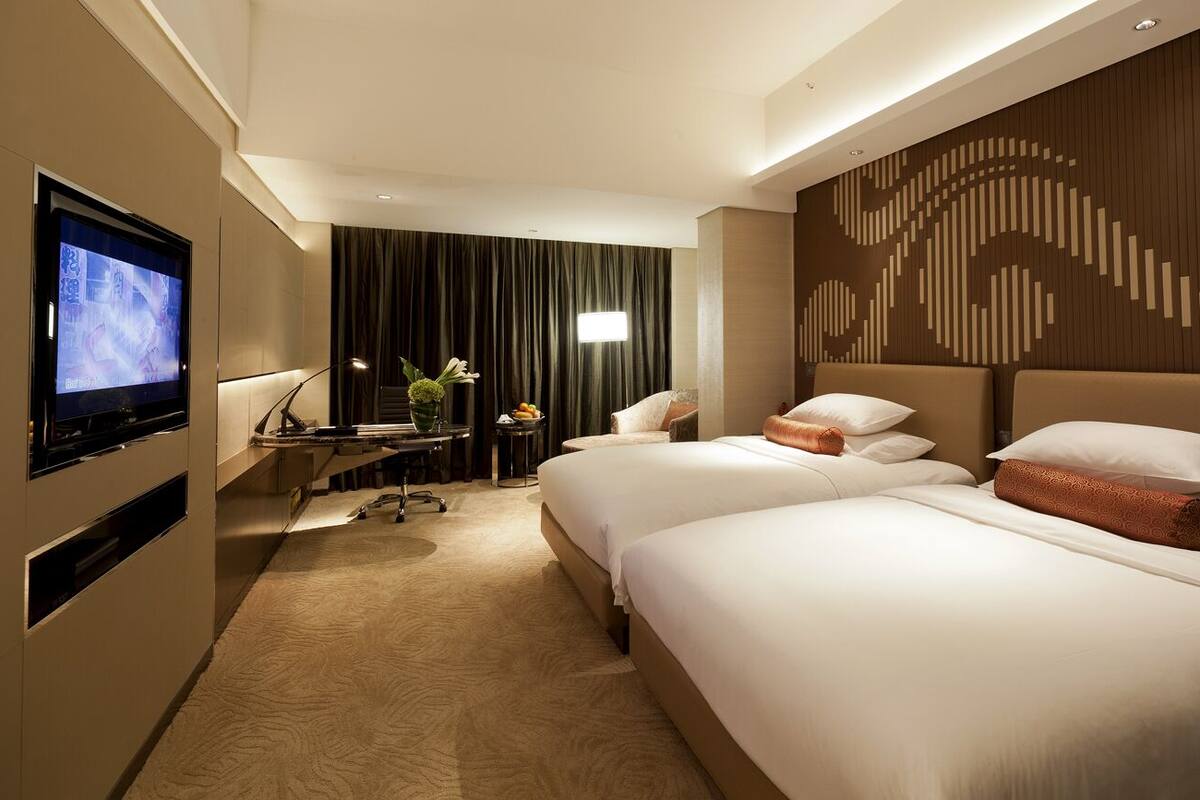 Une chambre d’hôtel avec deux lits, un bureau avec une chaise, un téléviseur à écran plat et un panneau décoratif mural.