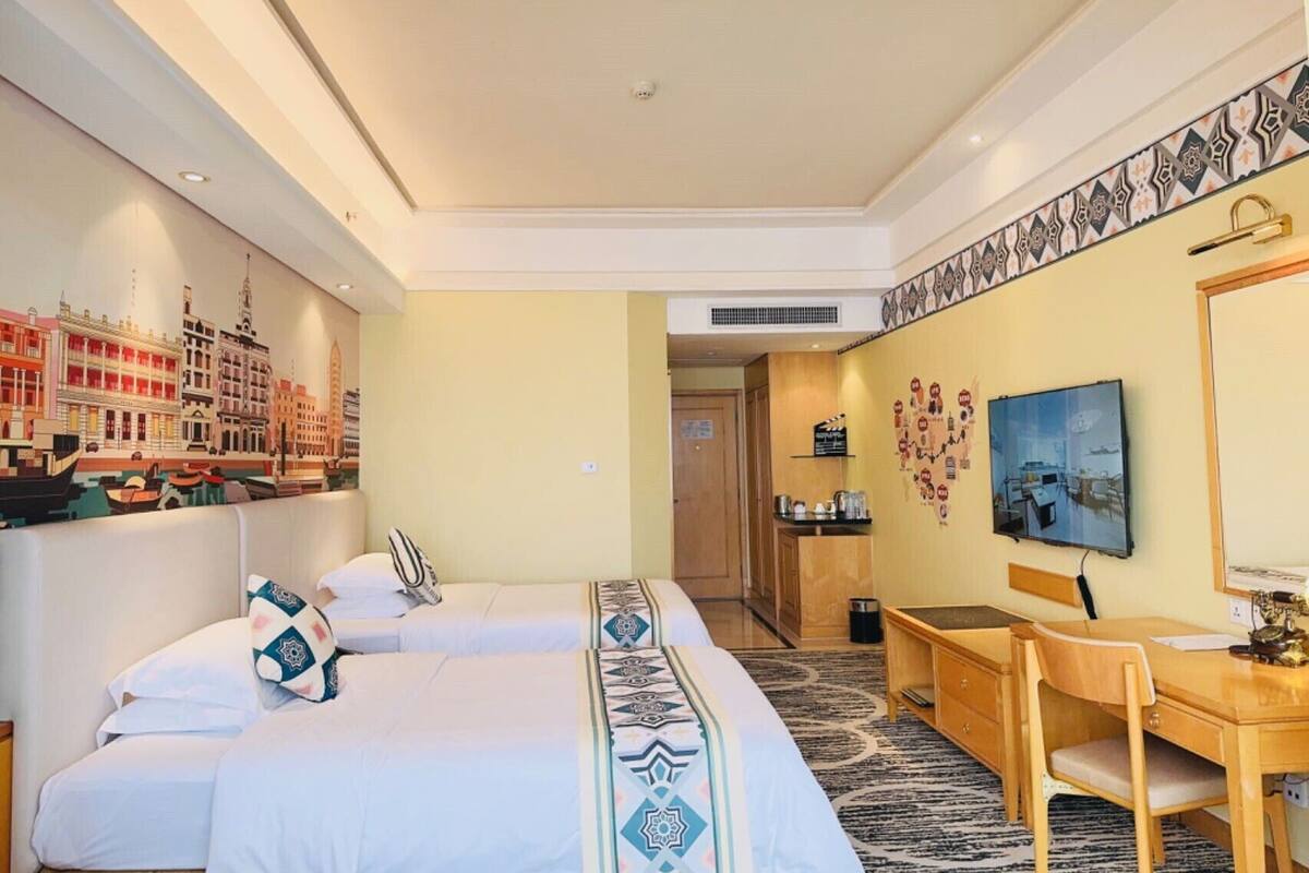 Une chambre d’hôtel avec deux lits, un bureau, une chaise, une télévision et une décoration murale.