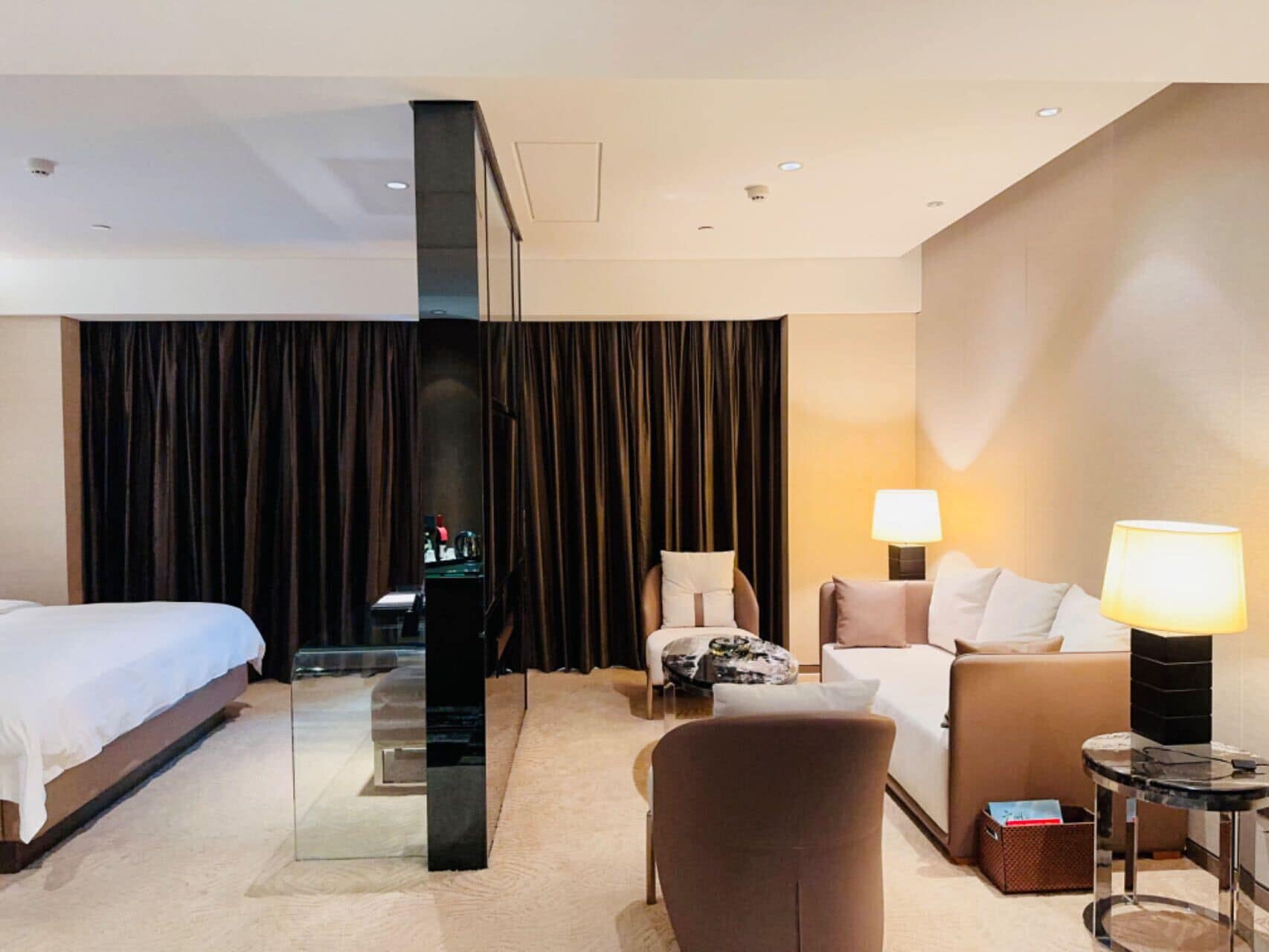 A hotel room with a bed, a sofa, a chair, a small table, and a lamp.