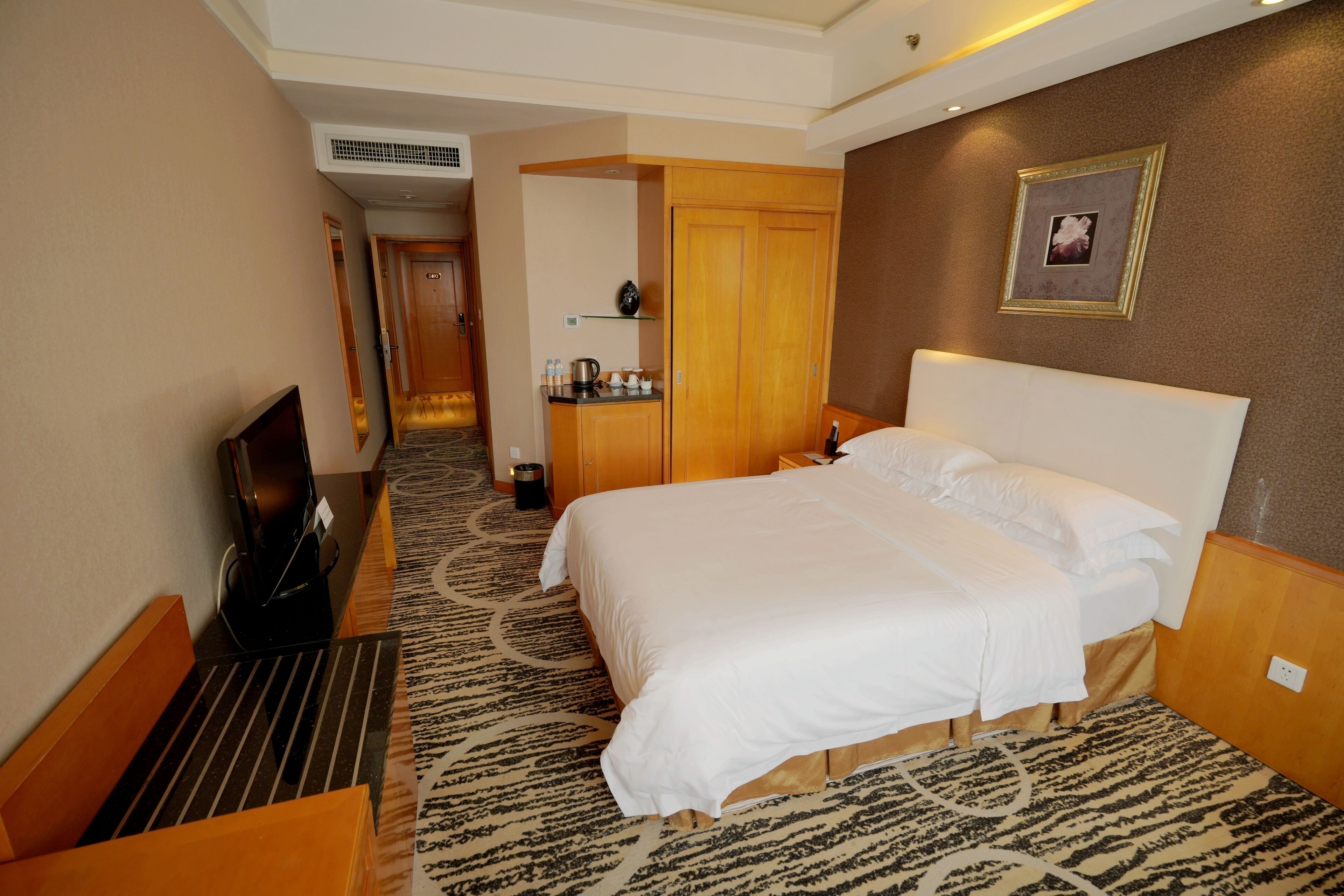 A hotel room with a bed, a desk with a television, a small kitchenette, and a bathroom.