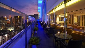 Un bar en la azotea con vistas a la ciudad, asientos al aire libre e iluminación ambiental.