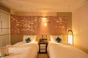 Habitación de hotel con dos camas, una mesita de noche, una lámpara fijada a la pared y un adornado en la pared con flores de cerezo y una luna.