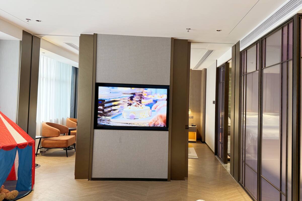 Une chambre d’hôtel dotée d’un téléviseur à écran plat fixé au mur, d’un coin salon avec des fauteuils et d’une grande fenêtre avec des rideaux.