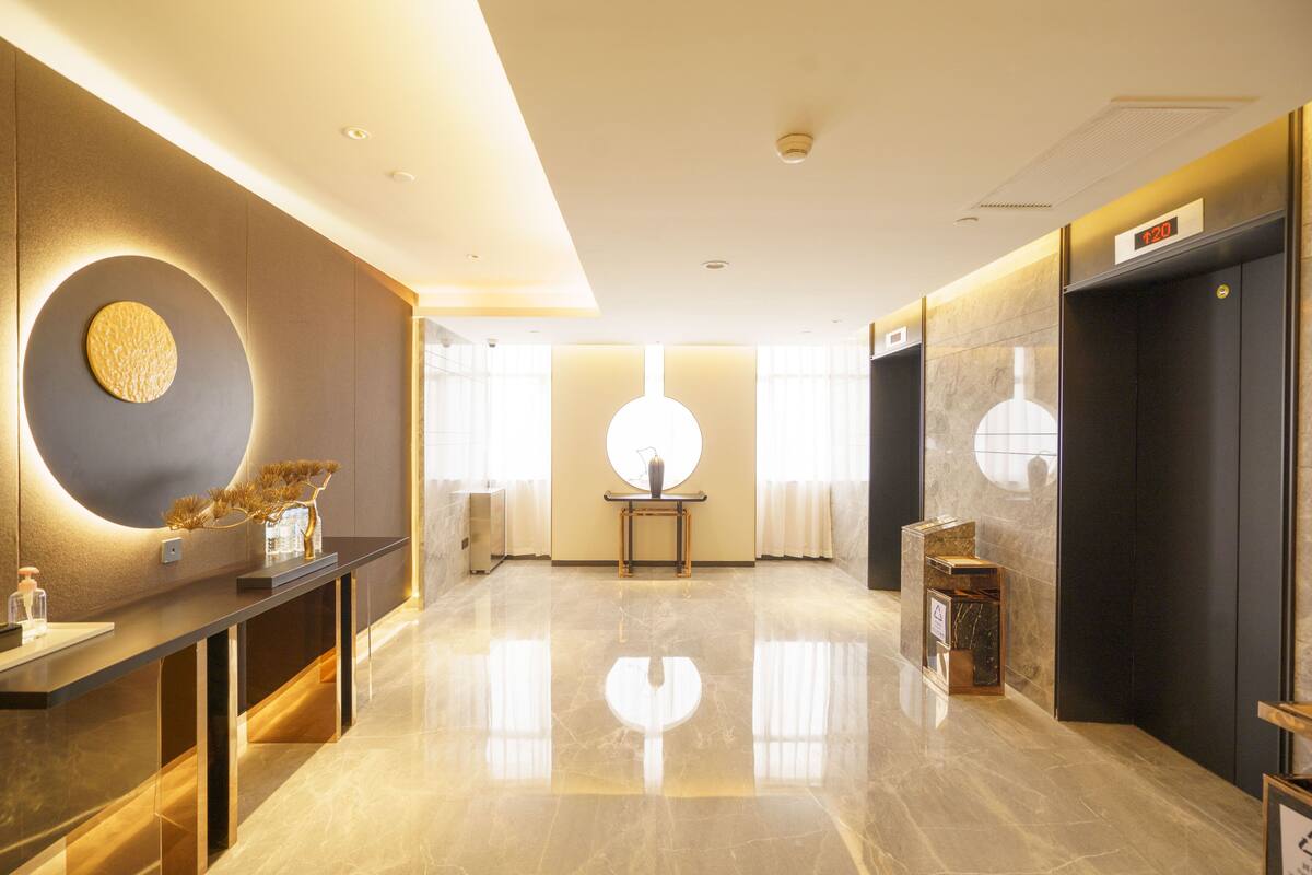 Un hall d’hôtel moderne avec un sol en marbre poli, un comptoir d’accueil, un élément décoratif circulaire au mur et un ascenseur.